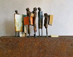 three metal figures standing on top of a rusted piece of metal with paint chippings