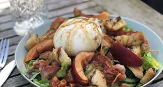 a white plate topped with lots of food on top of a wooden table next to a fork and knife