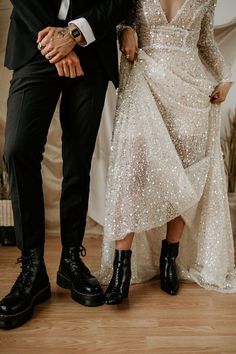 a man and woman standing next to each other in front of a white wall wearing black shoes