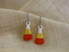 two pairs of earrings with red, yellow and white designs on them sitting on a piece of fabric