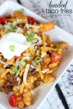 loaded taco fries in a square white dish with sour cream and green onions on top