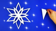 someone is cutting out a paper snowflake on a blue background with white stars