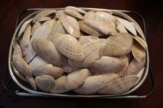 a metal container filled with clams on top of a wooden table