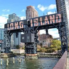 the long island sign is on top of an old bridge over water in front of tall buildings