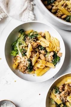 three bowls filled with pasta and vegetables on top of a white countertop next to two spoons