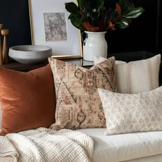 a couch covered in pillows next to a potted plant on top of a table