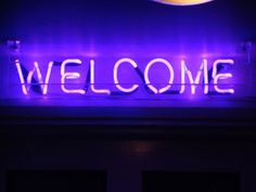 a neon sign that says welcome in front of a building with the moon above it