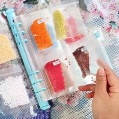 someone is holding up some plastic containers with different colored beads in them on a table