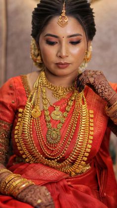 a woman in a red and gold sari with jewelry on her neck, smiling at the camera