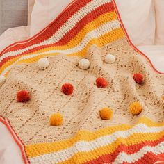 a crocheted blanket with pom - poms on it is laying on a bed