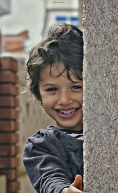 a young boy with braces is smiling and holding onto a cement wall in front of him