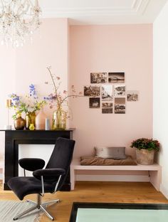 a living room with pink walls and pictures on the wall, a black chair in front of a table