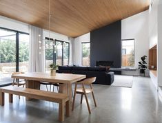 a large open living room and dining area with wood ceilinging, black couches, and wooden tables