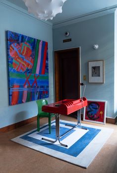 a red bench sitting in front of a painting on the wall next to a green chair