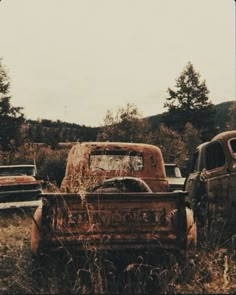 an old rusted truck sitting in the middle of a field with other trucks behind it