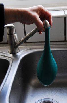 a person is holding a green vase over a sink faucet that has been turned upside down