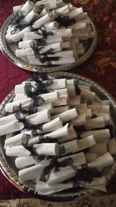 two silver plates with black and white napkins on them sitting on a red table cloth