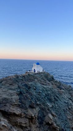 a small white building sitting on top of a rocky hill next to the ocean at sunset