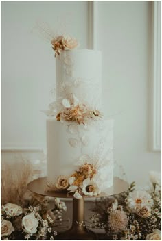 a three tiered white wedding cake with flowers on the side and gold decorations around it