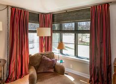 a living room with red curtains and a chair in front of a window that has a lamp on it