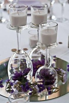 wine glasses and candles are arranged on a silver platter with purple flowers in them