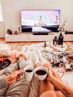 two people are sitting on the floor with cups of coffee in front of a flat screen tv