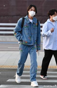 a man wearing a face mask walking across a street with another man in the background