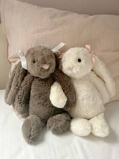 two stuffed animals sitting next to each other on top of a bed near a pillow