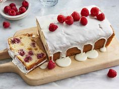 a cake with white frosting and raspberries on top sitting on a cutting board