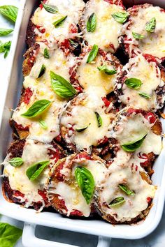 a casserole dish filled with meat, cheese and spinach garnished with fresh basil leaves