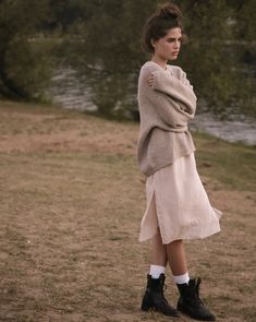 a woman is standing in the grass with her arms crossed and looking off into the distance