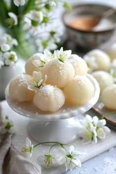 Delicate white mochi balls garnished with small white flowers, presented on a white pedestal. January Flavors, Fantasy Dessert Recipes, Fairy Desserts Ideas, Fantasy Snacks, Lemon Snowdrop Cookies, Fantasy Dessert, Rocky Mountain Snowdrops Recipe, Fancy Lemon Desserts, Fairy Desserts