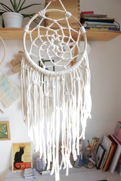 a white dream catcher hanging from a wooden shelf next to a bookcase and potted plant