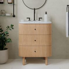 a bathroom with a round mirror above the sink and wooden cabinet below it, next to a potted plant