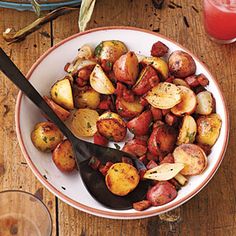 a white plate topped with potatoes next to a glass of red wine and a black spoon