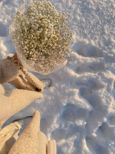 a person's feet in snow next to a flower pot with baby's breath