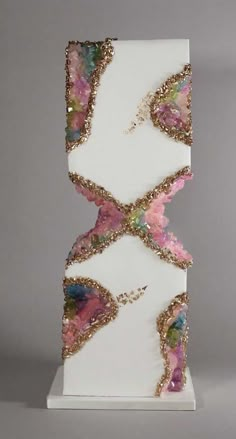 a white and pink sculpture with gold trimmings on it's sides, in front of a gray background