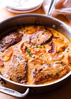 a pan filled with meat covered in gravy on top of a wooden table