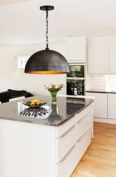 a kitchen with white cabinets and an island in front of a stove top oven under a large black pendant light