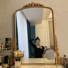 a woman taking a selfie in front of a large gold mirror on a dresser