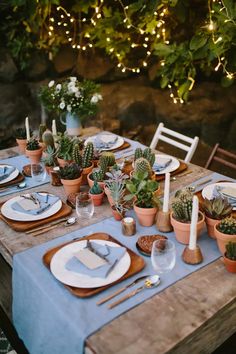 the table is set with plates, silverware and succulents in pots