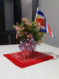 a vase filled with flowers sitting on top of a red place mat next to a flag