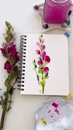 a notebook with flowers on it next to a pink vase and some other things that are sitting on the table