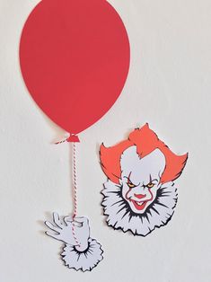 a red balloon with a clown face hanging from it's side next to a white wall