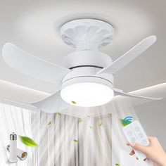 a person holding a remote control in front of a ceiling fan with green leaves on it