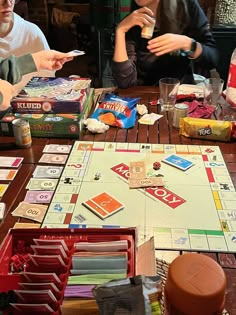 several people sitting around a board game on a wooden table with cards and other items