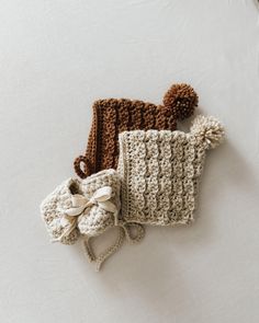 two crocheted hats and booties laying on top of each other, one with a bow