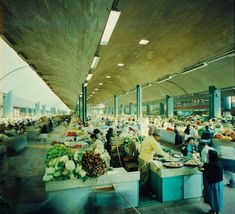 an indoor market with people shopping and selling fruits and veggies on the tables