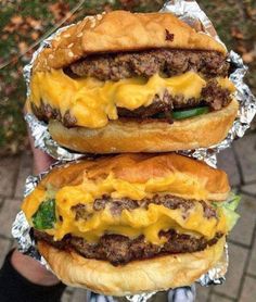 two hamburgers sitting on top of foil covered in cheese