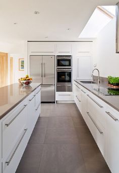 a modern kitchen with stainless steel appliances and white cabinetry, along with an open skylight